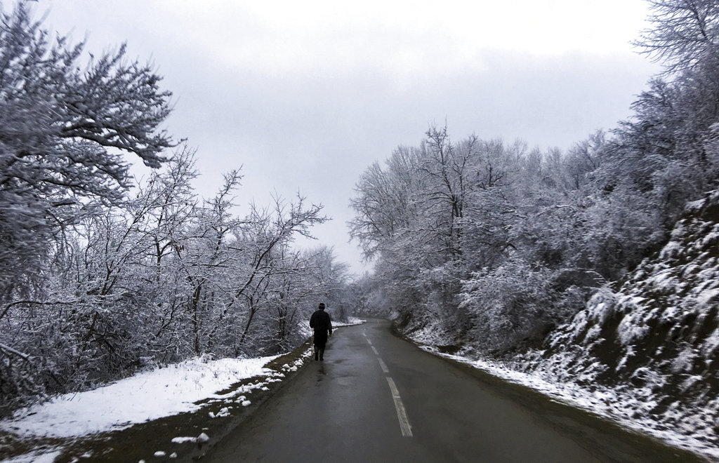 Shepherd walks down a snow covered road in the village of Brod, Kosovo on Thursday Jan. 18, 2018. (AP Photo/Visar Kryeziu)